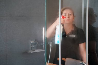 Hizmetçi banyoda duş bardak otel odasında siliyor. Temizlik. Kadın banyoda cam temizler