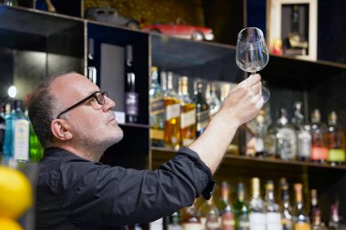 Yaşlı barmen cam temizler. Yakışıklı bir barmen bir bardak şarap bardakları parlatıyor. Hizmet kavramı.