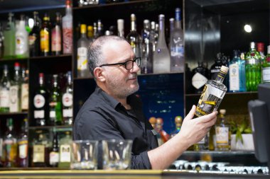 Yaşlı barmen bir şişe viski tutuyor. Barmen bir şişe viski inceliyor. Barmen viski istemciye otel barında içki alıyor. Hizmet kavramı. Barmen üzerinde konsantre.
