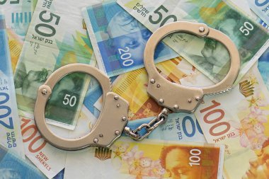 İsrail para arka plan üzerinde kelepçe. 50, 100 ve 200 Yeni İsrail para faturaları (banknot) şekel. Polis kelepçe. Mali suç, kirli para ve yolsuzluk kavramı.