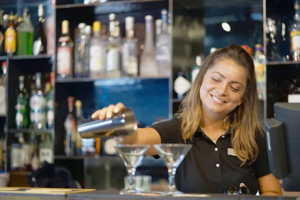 Professional bartender woman pours a fresh cocktail to the customers of the hotel bar. The bartender girl pours a cocktail. The concept of service. Focus on the bartender.