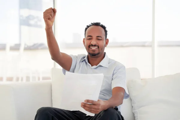 Happy entrepreneur man reading good news in a letter on sofa in home.