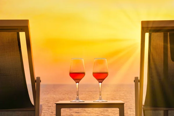 Wine glasses of red wine on the red background of the sea.