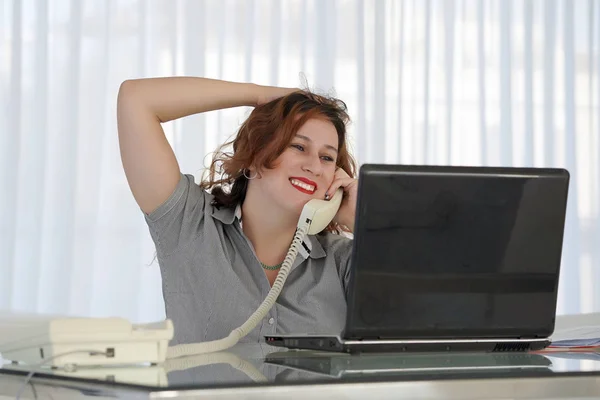 Женщина, сидящая за столом и отвечающая на телефонный звонок . Лицензионные Стоковые Изображения