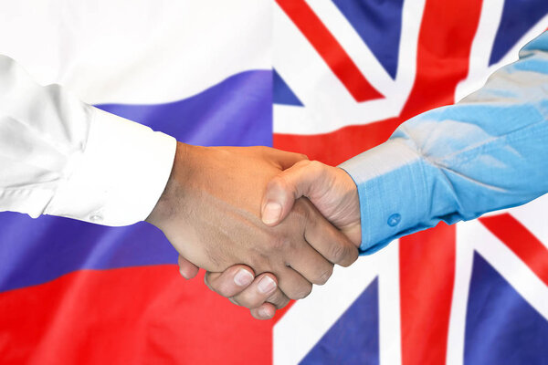 handshake on UK and Russia flag background.