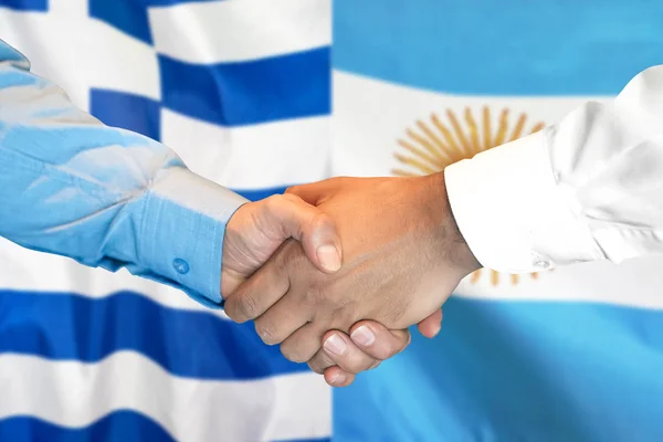 Aperto de mão no fundo da bandeira da Grécia e da Argentina . — Fotografia de Stock