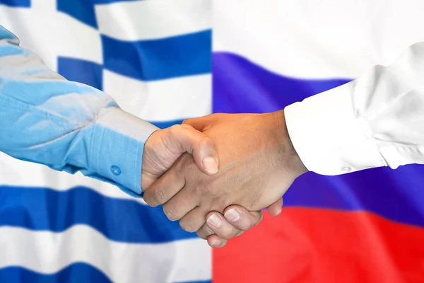 handshake on Greece and Russia flag background.
