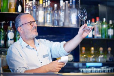 Barmen iş yerinde şarap bardağını siliyor.