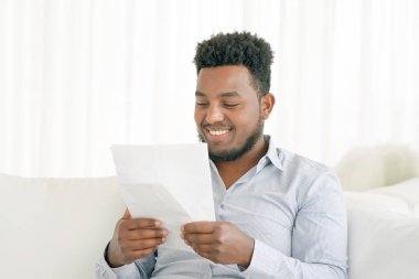 Mutlu girişimci adam evde kanepe bir mektupta iyi haber okuma. Adam yazılı olarak iyi haber zevk.