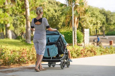 Bebek arabası olan kadın parkta yürüyor.