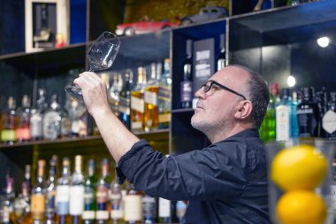 Barmen iş yerinde şarap bardağını siliyor.