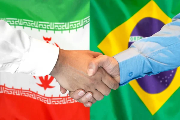 Apretón de manos sobre el fondo de la bandera de Irán y Brasil . — Foto de Stock