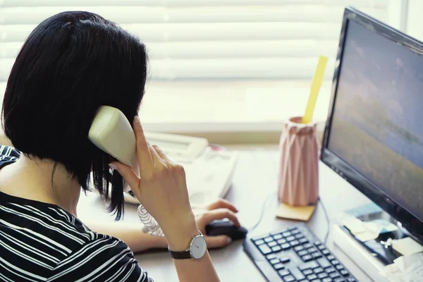 Mujer sentada en su escritorio trabajando y respondiendo una llamada telefónica . —  Fotos de Stock