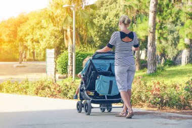 Bebek arabası olan kadın parkta yürüyor.