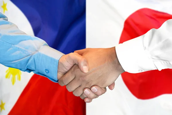 Handshake on Philippines and Japan flag background.