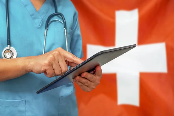 Surgeon or doctor using a digital tablet on the background of the Switzerland flag. Medical equipment or medical network, technology and diagnostics in Switzerland.