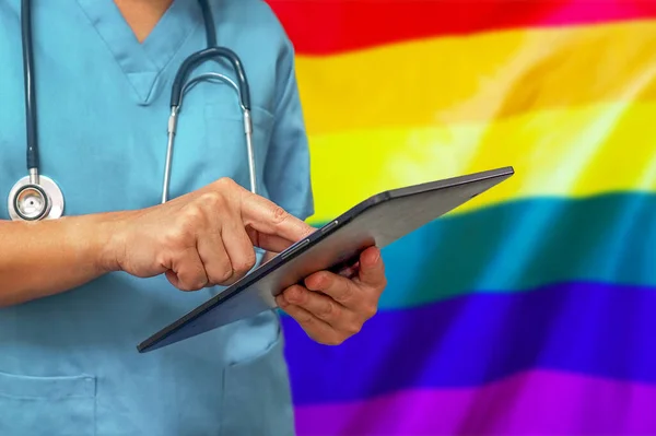 Doktor ya da cerrah LGBT gay bayrağının arka planında dijital tablet kullanıyor. Tıbbi teçhizat veya tıbbi ağ, teknoloji ve tanı.