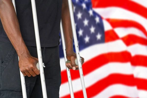 African man on crutches on the background of the USA flag. Disabled veterans of the US Army. The concept of violence and racism in USA