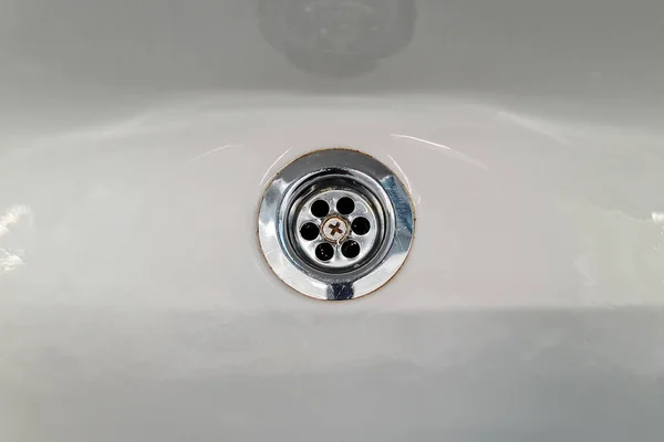 Chrome drain hole in sink. Fresh and clean white sink and silver water filter. Drain in a white clean sink, background, close-up