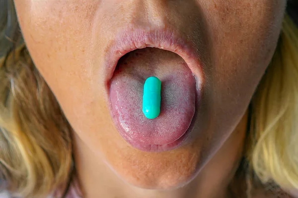 Blue pill on the tongue of a girl. Tablet on the tongue woman. Closeup Of Mouth Holding Vitamin Pill On Tongue. Vitamins And Supplements. Healthy Diet Nutrition, Health Concept.