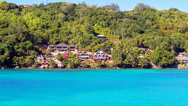 Houses and green vegetation on the coastline of the seychelles as seen from the azure blue waters