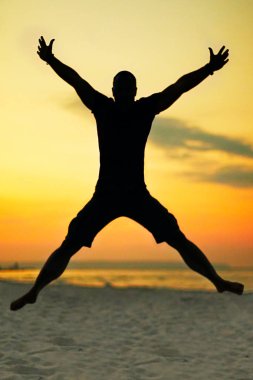 Bir X şeklinde havada atlama bir adam siyah silüeti. Arka planda bir parlak akşam gökyüzü güzel sarı ve turuncu renk ile olduğunu.