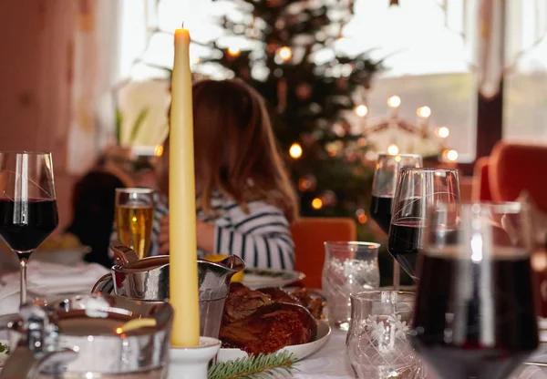 一个孩子坐在有盖的餐桌的背景下 转向冷杉树 桌子上覆盖着肉 红酒杯和蜡烛装饰 在背景中 你可以看到一棵有灯光的圣诞树 — 图库照片