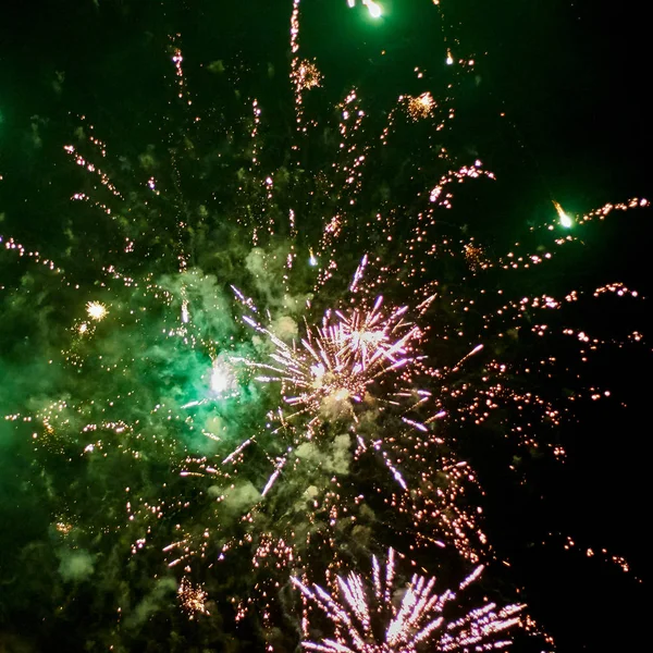 Fireworks rockets explode in the green illuminated night sky with lots of smoke and sparks