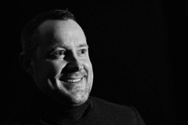 Gülümseyen genç 30 için 45 yaşındaki bir adam görünüyor, siyah bir zemin üzerine bir röportaj, siyah beyaz portre fotoğrafın o gibi görünüyor