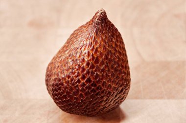 one Snake fruit Salak in detail on a wooden plate. You see the fine grain and structure of the skin of this ripe fruit, which looks like a snake. Vertical picture clipart
