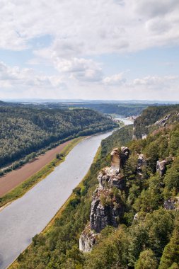 Elbe Vadisi 'ndeki Sakson İsviçre yürüyüş alanındaki Bastei bakış açısıyla ön planda yeşil ormanların arasında güzel bir kumtaşı oluşumu görülüyor.