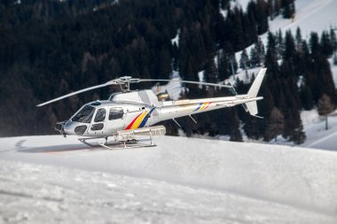 İtalyan Dolomiteleri 'ndeki bir kurtarma ekibinin gümüş rengi helikopteri karla kaplı helikopter pistinde bekliyor.