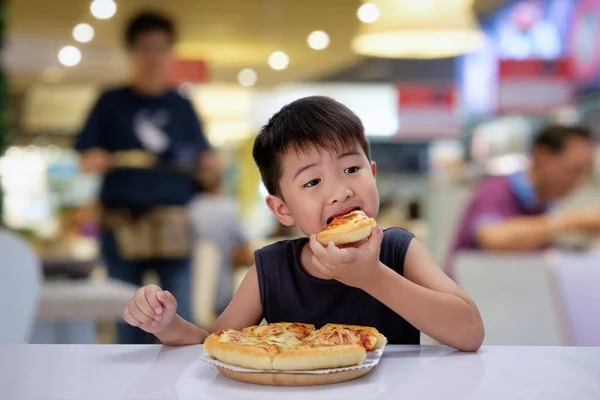 Asian 6-7 year boy is happy to eating pizza with a hot cheese melt stretched on a wooden pad in resturant.