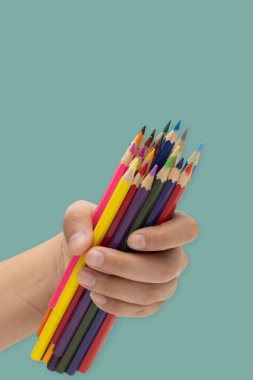 Yeşil bir arka plan üzerinde bir sürü kalem tutan eller.
