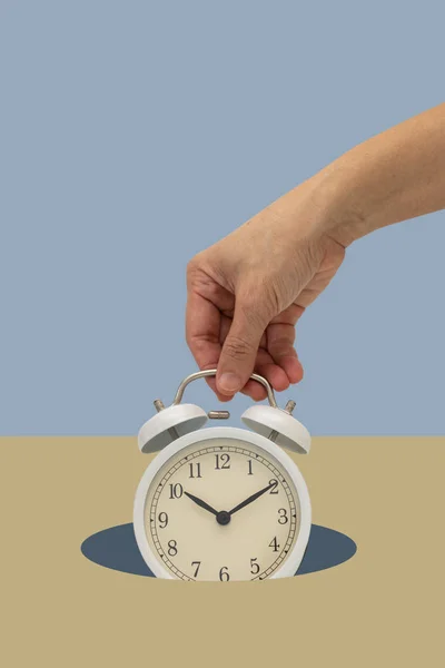 Mão segurando relógio de alarme vintage branco no fundo azul caindo — Fotografia de Stock