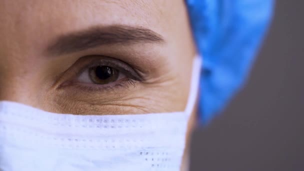 Medical nurse or scientist in surgical mask on blurred background in a COVID-19 hospital or lab. Macro shoot of a female surgeons eye. Doctor ready to take patient with coronavirus — Stock Video