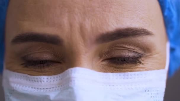 Женщина-хирург в защитной маске смотрит в камеру. Врач сопереживает пациенту Ковид-19, коронавирусный тест провалился. Уставший доктор выглядит расстроенным и расстроенным. — стоковое видео