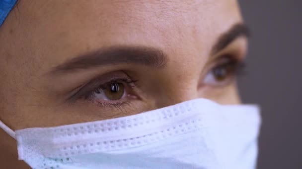 Χειρουργοί αντιμετωπίζουν σε μια ιατρική προστατευτική μάσκα, πλαϊνή όψη, κοντά. Επαγγελματίας υγείας φορώντας ένα χειρουργικό καπέλο, μάσκα, μάτια αναβοσβήνει αργά. Εργάτης υγείας στην πανδημία του Coronavirus Covid19 — Αρχείο Βίντεο