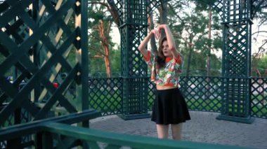 Sokakta telefonun önünde dans eden kız. Etekli ve parlak tişörtlü kız başvuru için dans hareketlerini tekrarlıyor. Dans yarışması. Farklı açılardan dans et. Güneşli bir günde oyukta dans etmek..