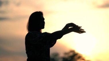Gün batımında dans eden kız. Göğüs göğüse. Altın gökyüzünün arka planında bir kızın karanlık silueti. Kontrast konsepti. Doğa konseptinde dans etmek. Kız nazik ama ritmik hareketler sergiliyor..