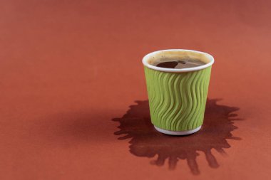 Kahverengi arka planda yeşil kağıt bardakta kahve lekeli. Masaya espresso döküldü. Kahve lekeli Americano bardağı. Kafede bir fincan kahvenin altına dökülmüş içki. Kahve dükkanı konsepti.