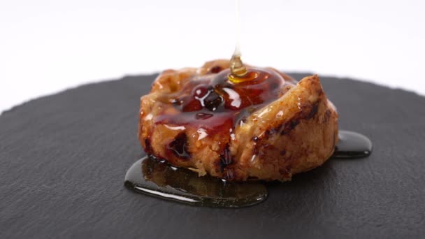 Honey is poured on fruit bun on round black rock stand on white background. Puff with fruit and honey in cafe. Tasty dessert concept. Sweets to order concept. Round cake on slate stand. Closeup. — Stock Video