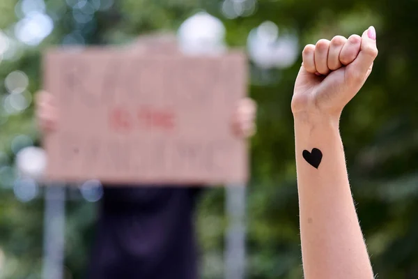 Kiev, Ucrânia - 31 de julho de 2020: punho levantado com coração negro no cartaz O racismo é o pano de fundo da pandemia. Pare o conceito de racismo. Black Lives Matter sinal de protesto. Acção contra a discriminação cor da pele. — Fotografia de Stock