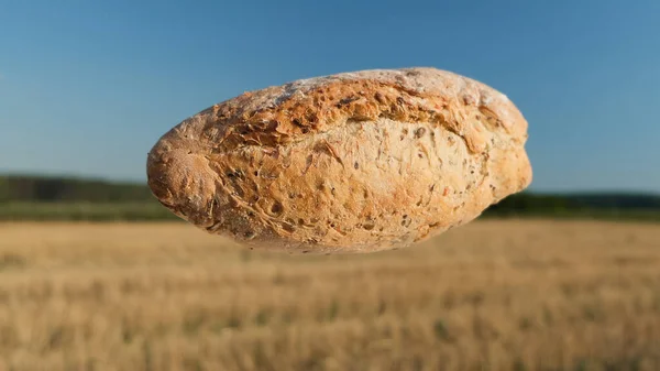 麦片在田边的空气中飘扬.自制烘焙概念。在干草和天空背景上烤新鲜面包.蓝色、绿色和黄色条纹背景的飞行面包. — 图库照片