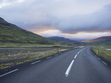 Asfalt yol eğrisi boş Kuzey yatay, yeşil çim renkli hills, su su birikintileri ve günbatımı dramatik gökyüzü, İzlanda Batı Highlands, kopya alanı dağlara yolu ile