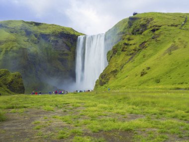 Güzel Skogafoss Güney İzlanda Skogar bir grup insan renkli giyinmiş turist, uzun pozlama hareket ile şelale bulanıklık, girintili kopyalama