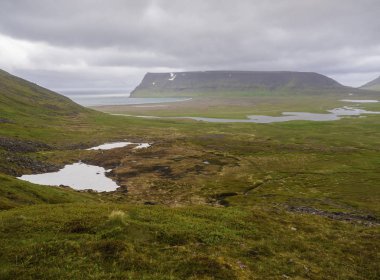 Kuzey yaz manzara, görünümü güzel kayalıklarla adalvik Cove Batı fjords doğada üzerinde rezerv İzlanda, Hornstrandir Nehri akış Deltası, kum plaj ve deniz, yamalı kar yeşil çayır ve kara bulutlar arka plan ile