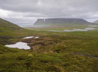 Northern summer landscape, View on beautiful cliffs in adalvik cove in west fjords nature reserve Hornstrandir in Iceland, with river stream delta, sand beach and sea, snow patched green meadow and dark clouds background clipart