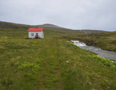 Patika terk edilmiş köyde Heysteri İzlanda Batı fjords uzak doğa rezerv Hornstrandir küçük beyaz evler kırmızı çatı, çiçeklerle yemyeşil yeşil çimen, nehir su cascade ve huysuz gökyüzü ile 