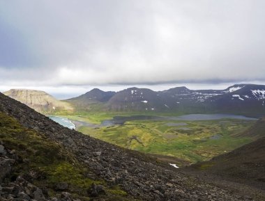 Kuzey yaz manzara, görünümü güzel kar üzerinde kayalıklarla ve fljotsvatn Gölü Hornstrandir, Batı fjords İzlanda, içinde Fljotavik Cove Nehri akış, yeşil çim çayır, moody gökyüzü arka plan ile kaplı